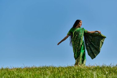 Yaz günü, özgün Hintli bir kadın mavi gökyüzünün altında yeşil alanda yürüyor.
