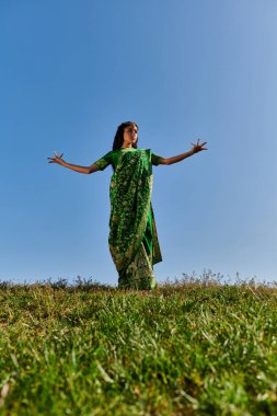 Geleneksel moda, sari giymiş genç Hintli kadın. Mavi gökyüzünün altında uzanan elleri var.