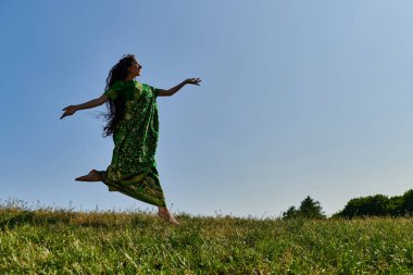 Mavi gökyüzünün altında yeşil çayırlarda koşan özgür fikirli Hintli kadın, mutlu yaz.