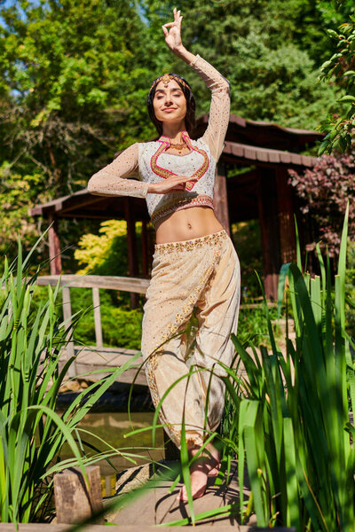 summer relax, elegant indian woman in traditional clothes dancing with closed eyes in green park