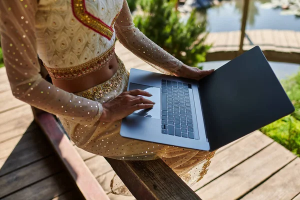 stock image cropped view of indian woman in traditional clothes networking, using laptop in summer park