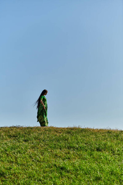 summer, ethnic heritage, young indian woman under blue cloudless sky in green field