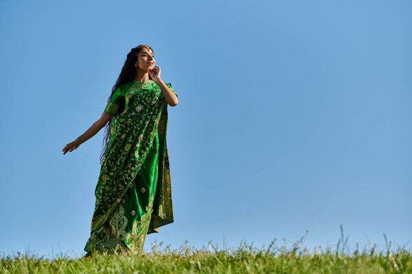 лето и природа, молодая индийская женщина в традиционной одежде смотрит вдаль под голубым и ясным небом