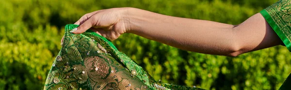 stock image partial view of young woman touching modern green sari with pattern near plants in park, banner