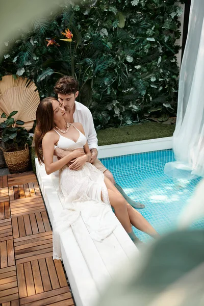 couple in white clothes sitting together near swimming pool during vacation, romantic getaway