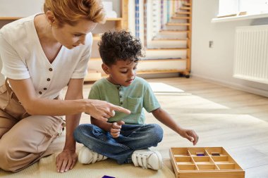 Montessori okulu, erken okul eğitimi, Afrika kökenli Amerikalı çocuğun yanındaki tahta kutuyu gösteren öğretmen.