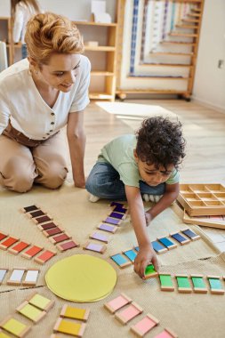 Montessori materyali, zeki Afrikalı Amerikalı çocuk mutlu bir kadının yanında eğitici renk oyunu oynuyor.