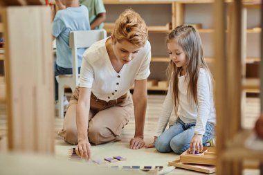 Montessori materyali, zeki kız sarışın öğretmenle eğitim oyunu oynuyor, erken okul eğitimi.
