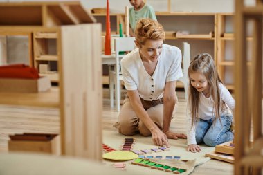 Montessori materyali, sarışın öğretmenle eğitim oyunu oynayan mutlu kız, erken okul eğitimi.