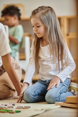 Montessori okulu, eğitim oyununun yanında oturan tatlı kız öğretmen, anaokulu öğrencisi, akıllı.