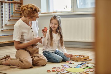 Montessori okulu, mutlu kız kadın öğretmenin yanında oturan ahşap bir eğitim oyunu parçası.