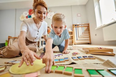 Montessori okulu, sarışın çocuk mutlu öğretmenin yanında eğitim oyunu oynuyor, hareket, renk eşleşmesi.