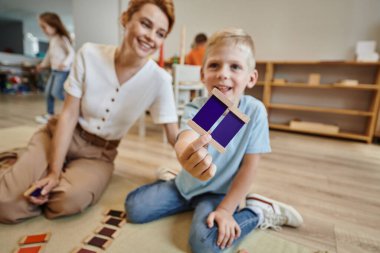 Montessori okulu, neşeli çocuk kadın öğretmenin yanında renk eşleştirme oyunu oynuyor, yerde oturuyor.