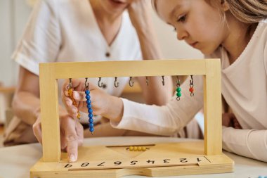 Montessori konsepti, öğretmenlerin yanındaki renkli boncuk merdivenlerle oynayan çocuk, ahşap tezgah, kapat.