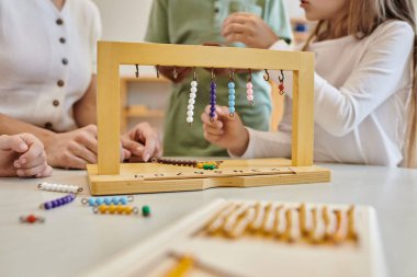 Renkli merdiven askısı, montessori konsept, öğretmenlerin yanında oyun oynayan çocukların kırpılmış görüntüsü.