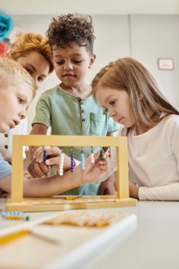 montessori konsepti, çok kültürlü çocuklar öğretmenlerin yanında renkli boncuk merdivenlerle oynuyorlar, çeşitlilik