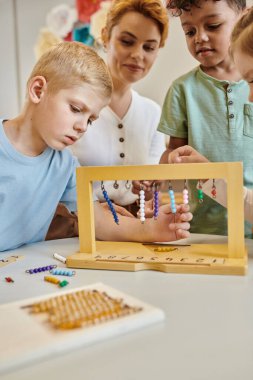Montessori okulu, çok kültürlü çocuklar öğretmenlerin yanında renkli boncuk merdivenlerle oynuyorlar, çeşitlilik...