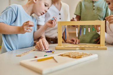 Montessori okulu konsepti, çok kültürlü çocuklar öğretmenlerinin yanında renkli boncuk merdivenlerle oynuyorlar.