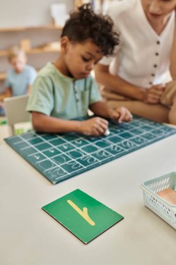 Öğretmen, Afrika kökenli Amerikalı çocuğun tahtaya yazı yazdığını, saydığını, oyun oynayarak öğrendiğini gözlemliyor.