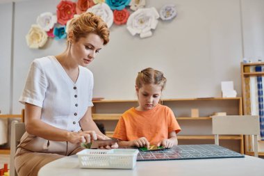 Akıllı kız, kadın öğretmenin yanında sayıyor, yazı tahtası, Montessori okulunda saymayı öğreniyor.