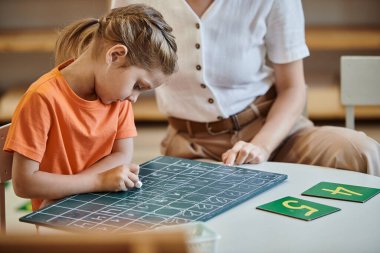 Rakamların yakınındaki tahtaya yazı yazan tatlı kız oyun, öğretmen, Montessori konsepti ile öğreniyor.