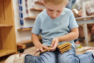 Sarışın çocuk, Montessori boncuklarını tutuyor, sayıyor, oyun oynayarak öğreniyor, erken eğitim alıyor.