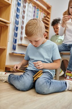 Sarışın çocuk Montessori boncuklarını tutuyor, sayıyor, oyun yoluyla öğreniyor, çeşitli çocuklar