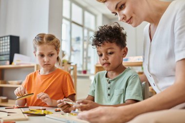 Irklar arası çocuklar didactik montessori malzemeleriyle oynuyorlar. Kadın öğretmenlerin yanında, çeşitlilik