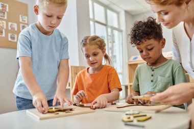 Okuldaki öğretmenin yanında didactic montessori malzemesiyle oynayan ırklar arası çocuklar, öğrenin ve oynayın.