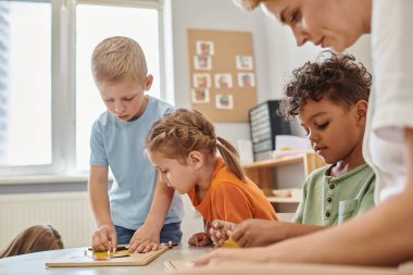 Montessori okulunda didactic materyallerle oynayan öğretmen ve çok ırklı çocuklar