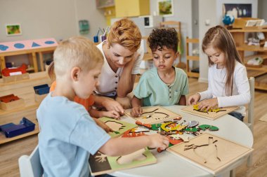 Öğretmen, Montessori okulunda oyun masasında birlikte oynayan ırklar arası çocuklarla konuşuyor.