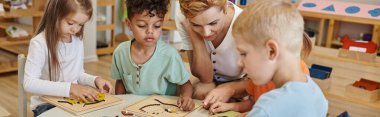 Öğretmen Montessori okulunda çoklu etnik çocuklarla oynarken didactic materyal kullanıyor, afiş