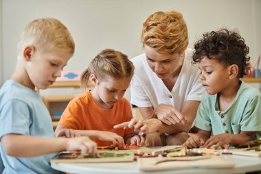 Öğretmen Montessori okulunda didactic materyallerin yakınında çok ırklı çocuklarla konuşuyor.