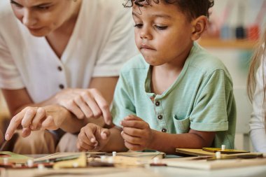 Montessori okulunda ders sırasında öğretmenin yanında oynayan Afrikalı Amerikalı çocuk.