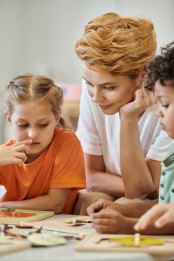 Çocuk, Montessori okulunda çocuğun yanında öğretmenle konuşuyor.