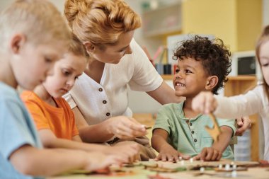 Öğretmen, çocuklar Montessori okulunda oynarken gülümseyen Afrikalı Amerikalı çocukla konuşuyor.
