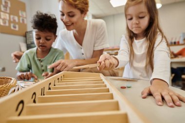 Montessori okulunda öğretmenlerin yanında tahta çubuklarla oynayan çok ırklı çocuklar.