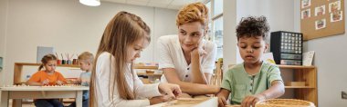 Montessori okulunda ders sırasında çocukların yanında oturan öğretmen, afiş.