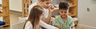 Öğretmen Montessori okulunda derste neşeli ırklar arası çocuklar hakkında konuşuyor.