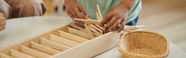 partial view of african american boy holding wooden sticks during lesson in montessori class, banner clipart