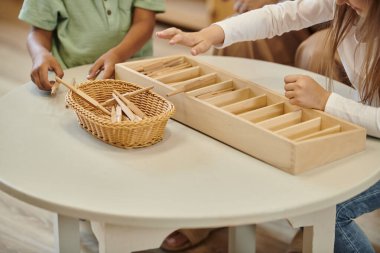Montessori okulunda ders sırasında tahta sopalarla oynayan çoklu etnik kökenli çocuklar.