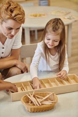 Öğretmen, Montessori okulunda oynarken gülümseyen ırklar arası çocuklarla konuşuyor.