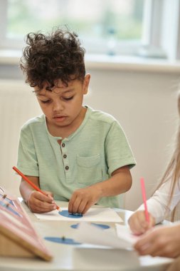 Afrika kökenli Amerikalı çocuk kurşun kalemle acı çekiyor ve Montessori sınıfında bulanık öğretmen.