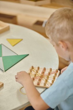 Montessori okulunda ders sırasında lastik bant ve tahta çubuklarla oynayan bir çocuk.