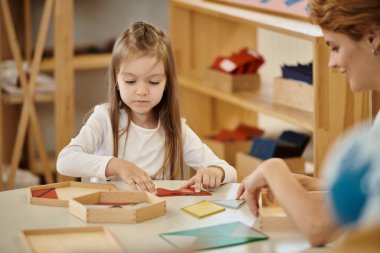 Gülümseyen öğretmen Montessori okulunda kız ve didactic malzemelerle oynuyor.