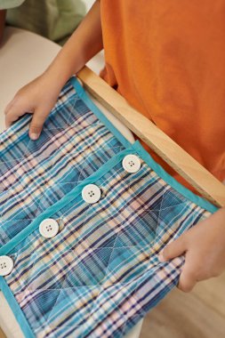 Montessori okulunda ders sırasında elinde düğmeli kumaş ve düğme olan kız manzarası.