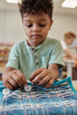 Bulanık Afrikalı Amerikalı çocuk Montessori okulunda kumaş ve düğmelerle oynuyor.