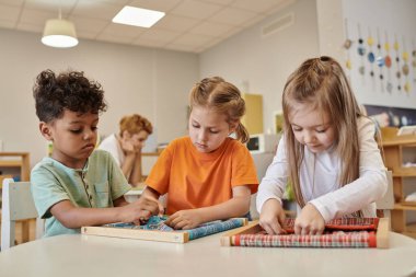 Montessori okulunda kumaş ve düğmelerle oynayan çok ırklı çocuklar.