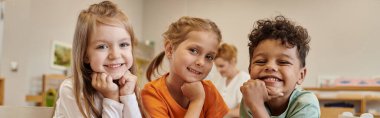 Montessori okulunda bulanık sınıflarda kameraya gülümseyen ve ırklar arası çocuklar, afiş.