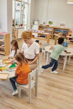 Gülümseyen öğretmen Montessori okulunda çoklu etnik çocukların yanında çocuklarla oynuyor.